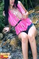 Seated on riverbank wearing pink top exposing breast